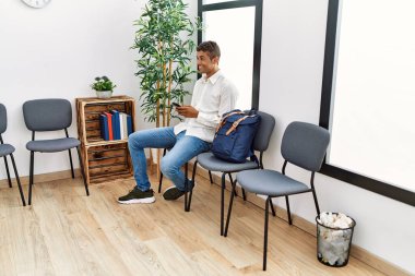 Bekleme odasında akıllı telefon kullanan genç bir İspanyol bekliyor.