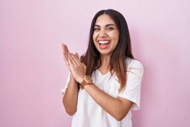 Young arab woman standing over pink background clapping and applauding happy and joyful, smiling proud hands together 