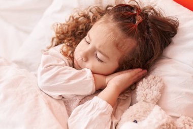 Sevimli sarışın bebek yatak odasında oyuncak ayıyla yatıyor.