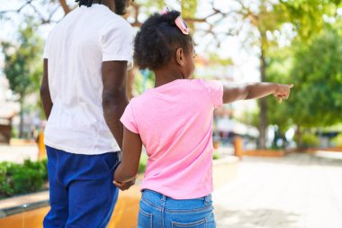 Father and daughter walking with hands together pointing with finger at park
