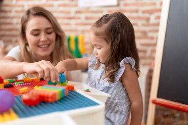 Teacher and toddler playing with construction blocks sitting on table at kindergarten