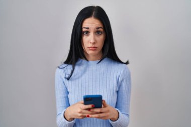 Hispanic woman using smartphone skeptic and nervous, frowning upset because of problem. negative person. 
