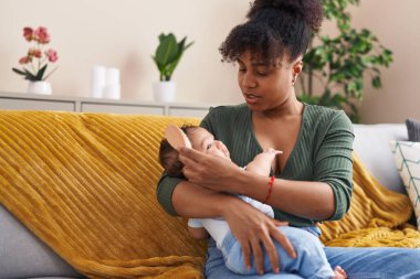 Anne ve oğlu evdeki kanepede oturup saçlarını tarıyor.