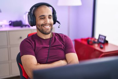 Young latin man streamer smiling confident sitting with arms crossed gesture at gaming room
