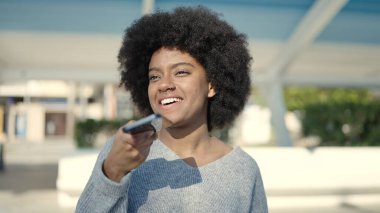 Afro-Amerikalı kadın gülümsüyor. Parktaki akıllı telefondan konuşuyor.