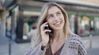 Genç sarışın kadın gülümsüyor. Kendine güveni tam. Akıllı telefondan konuşuyor.