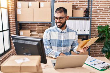 Genç bir İspanyol iş adamı ofiste dizüstü bilgisayarla paket tutuyor.