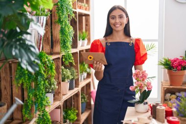 Young beautiful hispanic woman florist holding envelope letter and plant at florist