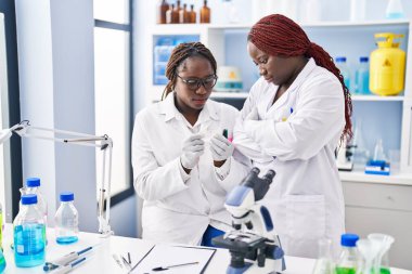 African american women scientists looking sample standing with arms crossed gesture at laboratory