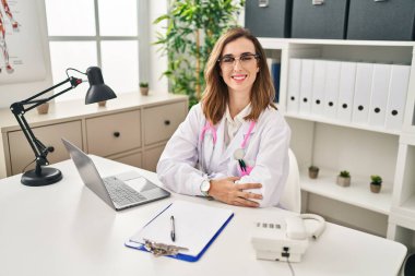 Klinikte çalışan doktor üniforması giyen genç bir kadın.