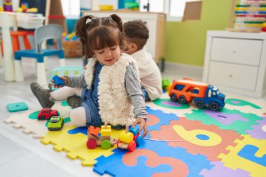 Brother and sister playing with cars toy sitting on floor at kindergarten