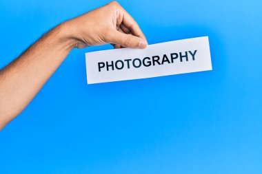Hand of caucasian man holding paper with photography word over isolated blue background