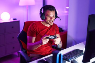 Young hispanic man streamer playing video game using joystick at gaming room