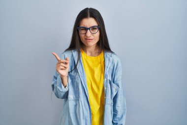 Mavi arka planda dikilen genç İspanyol kadın endişeli ve endişeli bir ifadeye işaret ediyor. 