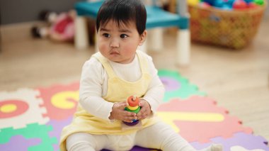 Adorable hispanic baby playing with hoops sitting on floor at kindergarten