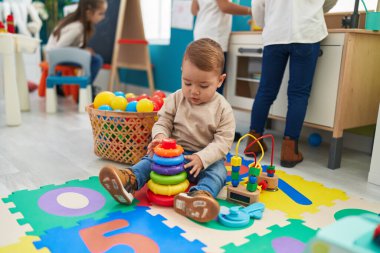 Adorable blond toddler playing with hoops toy sitting on floor at kindergarten