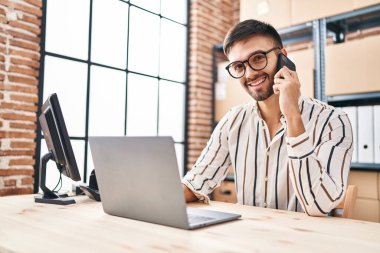 Genç İspanyol iş adamı. Ofiste bilgisayarla akıllı telefondan konuşuyor.