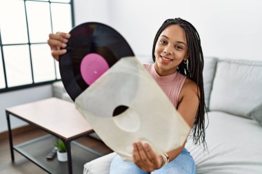 Genç Afrikalı Amerikalı kadın gülümsüyor. Elinde vinil disk tutuyor.