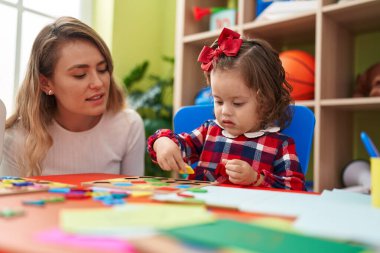 Teacher and toddler playing with maths puzzle game sitting on table at kindergarten