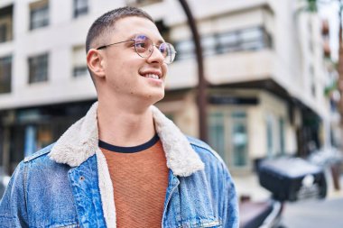 Young hispanic man smiling confident looking to the side at street