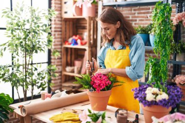 Young beautiful hispanic woman florist cutting plants at florist