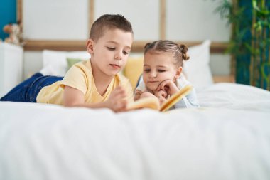 Two kids reading story book lying on bed at bedroom
