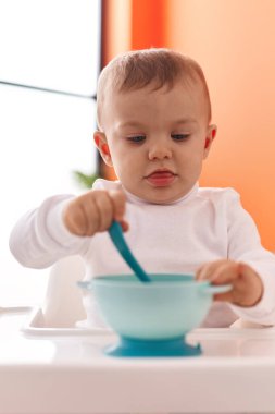 Sevimli sarışın çocuk sandalyeye oturmuş, evde yemek yemek için bekliyor.