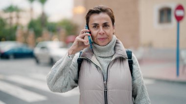 Orta yaşlı İspanyol kadın gülümsüyor. Akıllı telefondan konuşuyor.