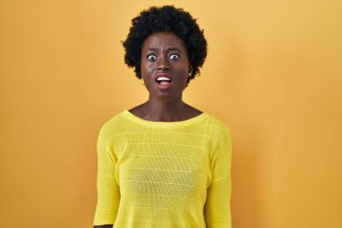 African young woman standing over yellow studio angry and mad screaming frustrated and furious, shouting with anger. rage and aggressive concept. 
