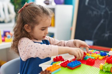 Adorable blonde girl playing with construction blocks sitting on table at kindergarten