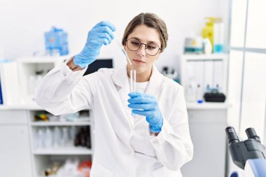 Laboratuvarda pipet kullanan, bilim adamı üniforması giyen İspanyol genç bir kadın.