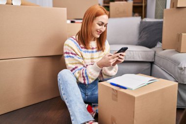 Young caucasian woman using smartphone sitting on floor at new home