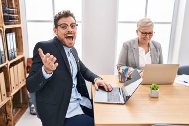 Hispanic young man working at the office celebrating achievement with happy smile and winner expression with raised hand 