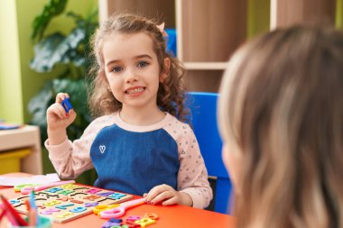 Adorable blonde girl playing with maths puzzle game sitting on table at kindergarten