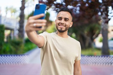 Genç İspanyol adam gülümsüyor. Parktaki akıllı telefonun yanında özçekim yapıyor.