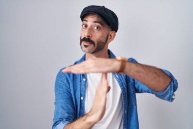 Hispanic man with beard standing over isolated background doing time out gesture with hands, frustrated and serious face 