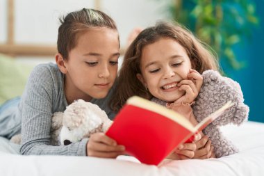 Two kids reading story book lying on bed at bedroom