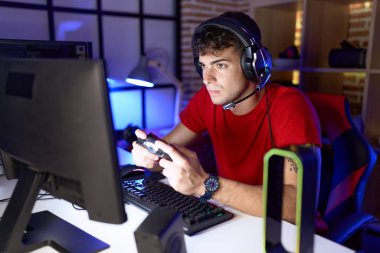 Young hispanic man streamer playing video game using joystick at gaming room