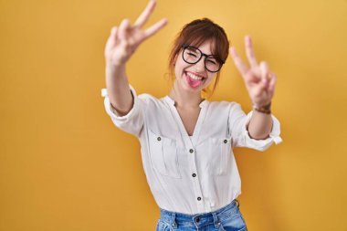 Sarı arka planda rahat gömlekler giyen genç ve güzel bir kadın. İki elini de zafer işareti yaparken göstererek gülümsüyor. İki numara.. 