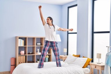 Young man standing on bed dancing at bedroom