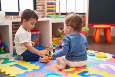 Anaokulunda yerde oturmuş oyuncaklarla oynayan iki çocuk.