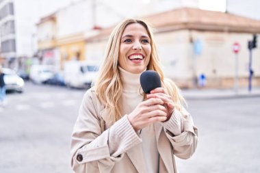 Young blonde woman reporter working using microphone at street