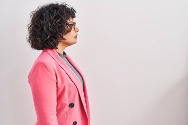 Kıvırcık saçlı İspanyol kadın, yalıtılmış arka planda duruyor, yan yana bakıyor, rahat poz veriyor, kendine güvenen bir gülümsemesi var.. 