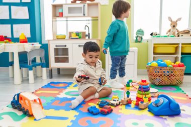 Two kids playing with cars toy sitting on floor at kindergarten