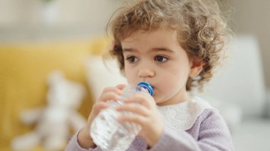 Adorable hispanic girl drinking water standing at home