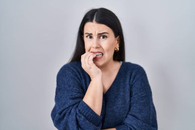 Tecrit edilmiş arka planda duran genç esmer kadın elleri ağzında tırnak yerken gergin ve stresli görünüyor. anksiyete. 