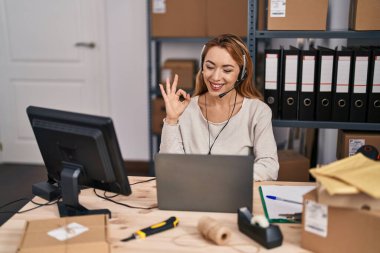 Hispanic woman working at small business ecommerce wearing headset doing ok sign with fingers, smiling friendly gesturing excellent symbol 