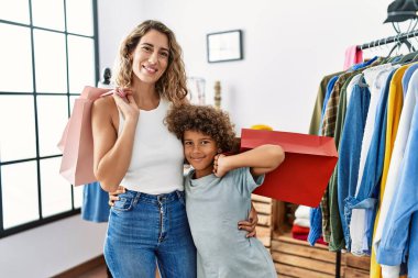 Mother and son smiling confident and hugging each other holding shopping bags at clothing store