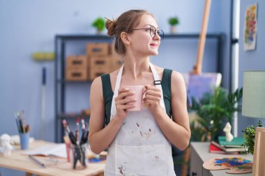 Young caucasian woman artist drinking coffee standing at art studio