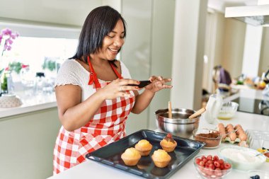 Hispanic brunette woman taking photo of chocolate muffins at the kitchen